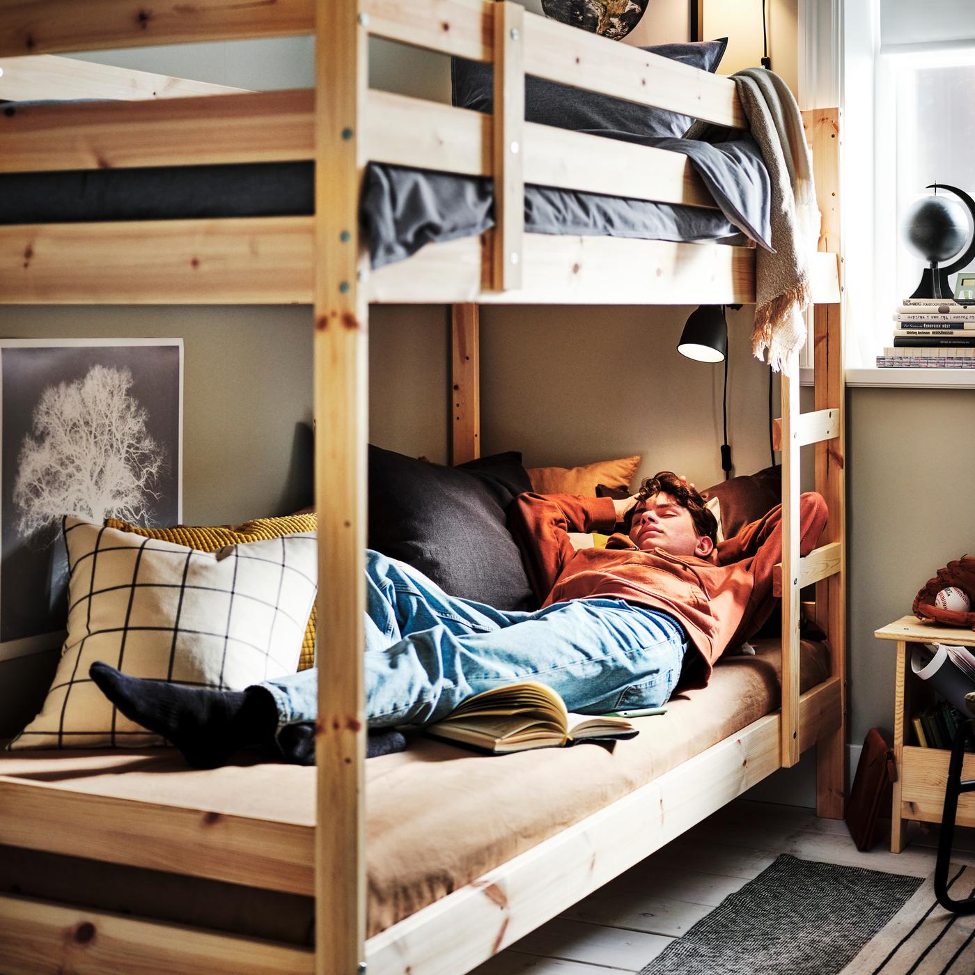 Ein Teenager schläft in einem MYDAL Etagenbettgestell in Kiefer. Das obere Bett ist mit dunkelblauer KOPPARBLAD Bettwäsche bezogen.