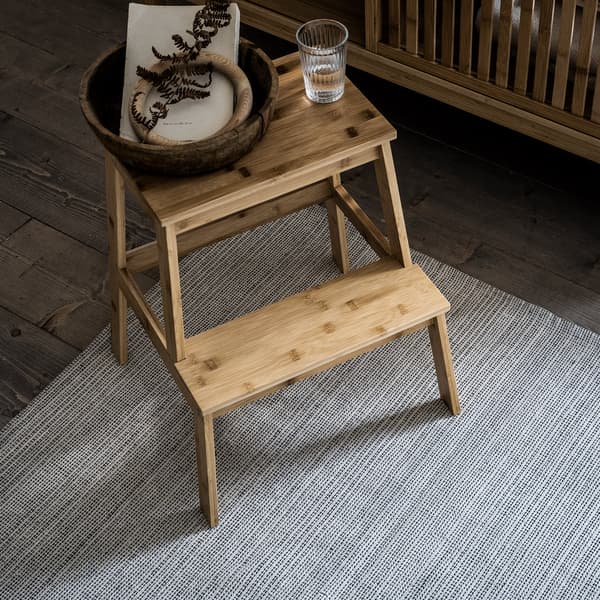 Ein Tritthocker aus Bambus steht auf einem hellgrauen Teppich.