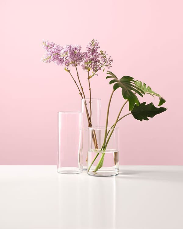 Ein Vasen-Set mit Blumen auf einem Tisch vor einer rosa Wand.