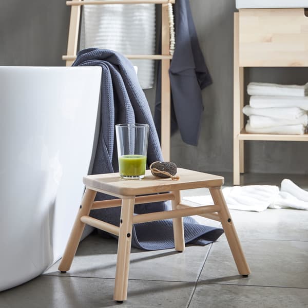 Ein VILTO Badezimmerhocker neben einer Badewanne. Darauf steht ein Glas mit grünem Smoothie.