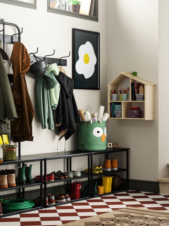 Ein Vorzimmer mit einem gemusterten Teppich, Garderobenmöbel in schwarz, einem Bild auf der Wand und einem Regal in einer Hauform.