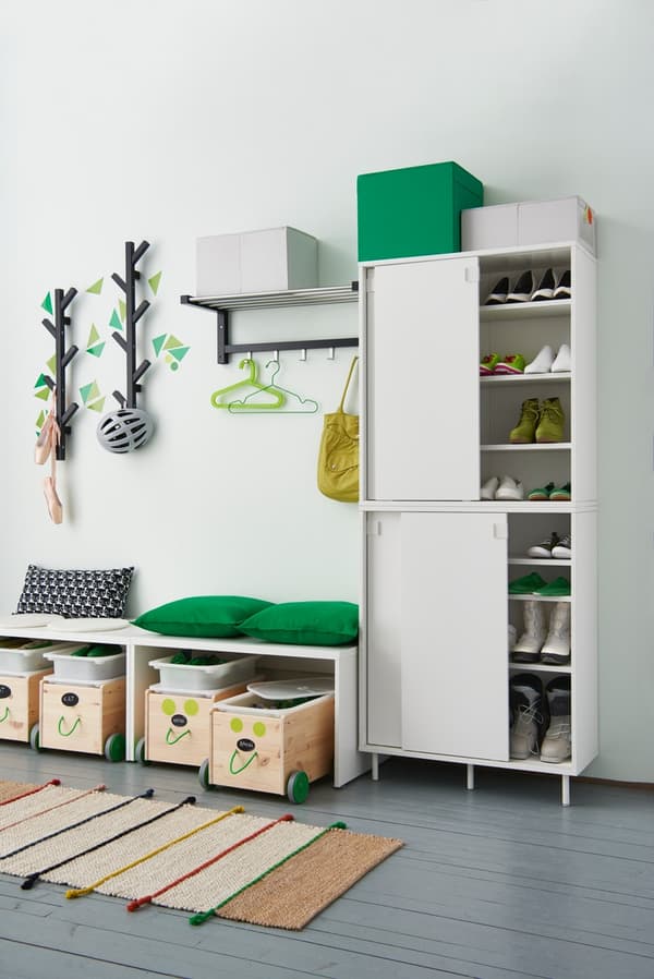 Ein Vorzimmer mit zwei übereinandergestapelten, weißen Schränken mit Schuhen auf Einlegeböden, Boxen mit Kinderschuhen unter Bänken und Aufhängungen an der Wand
