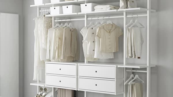 Ein weißer ELVARLI Kleiderschrank steht an einer weißen Wand. Diese hat in der mitte 4 Schubladen und auf der Seite Kleiderstangen.
