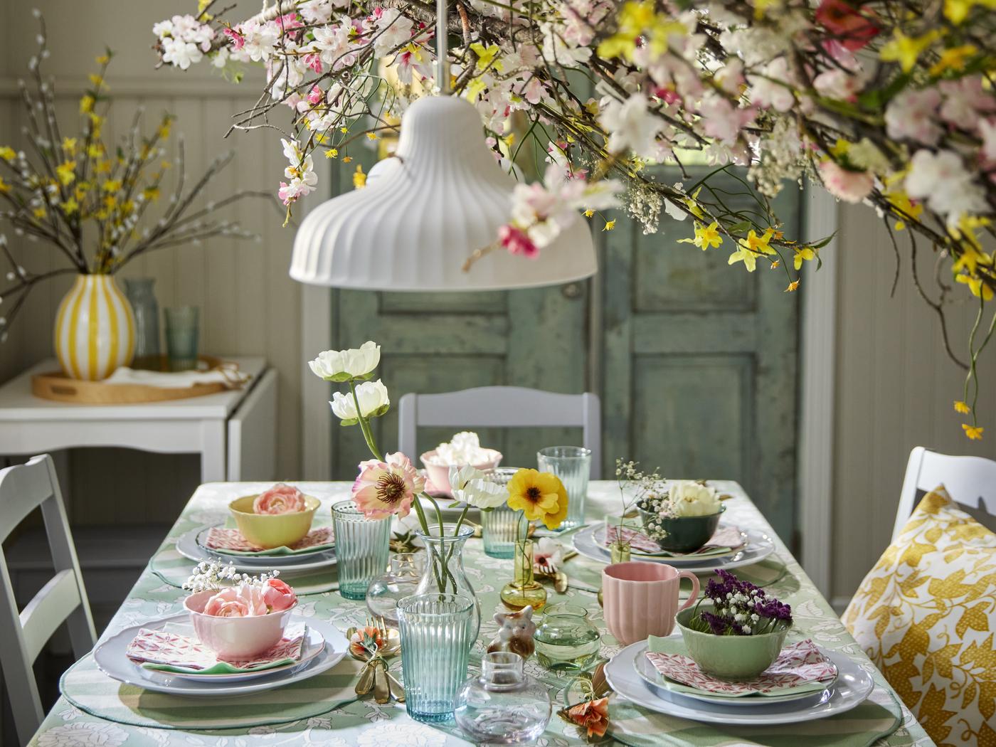 Ein weißer Esstisch, gedeckt, sehr bunt, viele Pastellfarben, Blumen und florale Muster