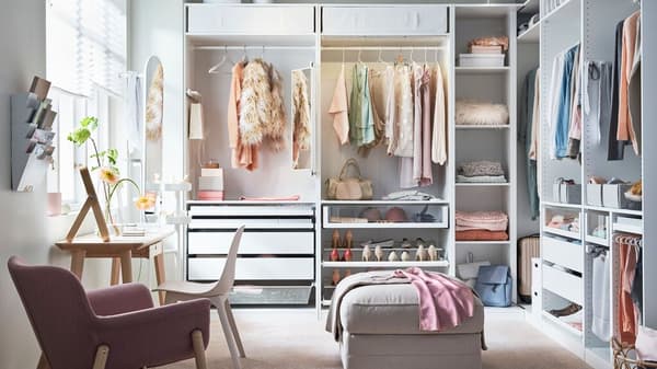 Ein weißer PAX Kleiderschrank steht in einem hellen Raum. Er hat keine Türen und man kann sehen das dieser Kleiderschrank sehr schön eingerichtet ist.