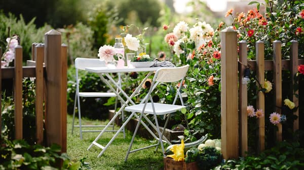 Ein weißer TORPARÖ Tisch und zwei TORPARÖ Stühle sind hier in einem sonnigen, romantischen Garten zwischen Blumenbeeten zu sehen.