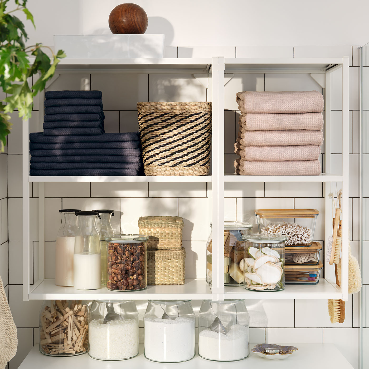 Ein weißes ENHET Regal mit offenen Fächern, in denen Hantücher und Vorratsbehälter aus Glas stehen.