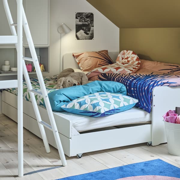 Ein weisses SLÄKT Bettgestell mit Unterbett + Aufbewahrung, bei dem das Unterbett hervorgezogen und zum Übernachten hergerichtet ist. Auf dem Bett ist ein Stofftier zu sehen.
