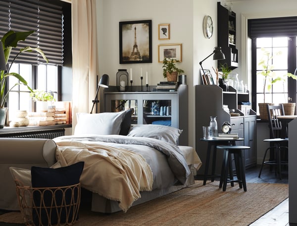 Ein Wohnzimmer, in dem das Bettsofa zum Schlafen vorbereitet ist. In der Nähe stehen eine graue HAUGA Vitrine und graue HAUGA Schränke mit Türen.