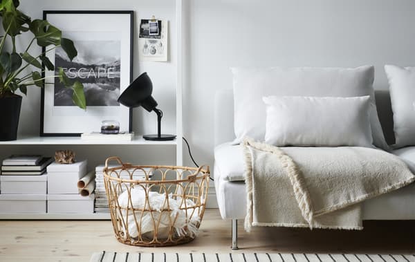 Ein Wohnzimmer mit einem weissen Sofa, einer schwarzen Leuchte, offener Aufbewahrung und Weidenkörben voller Plaids