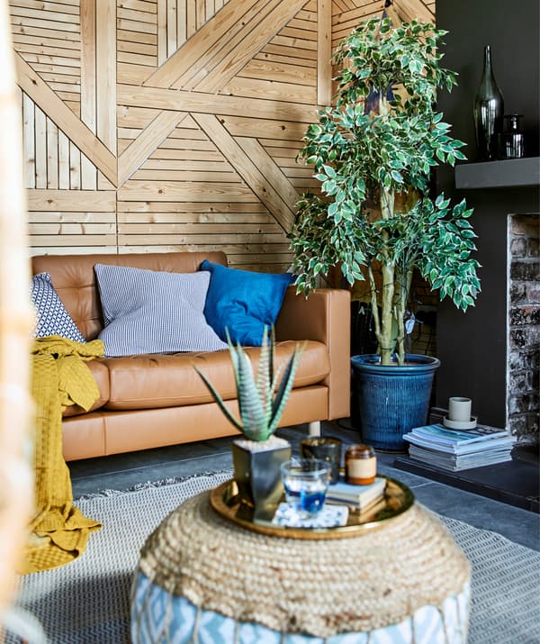 Ein Wohnzimmer mit holzverkleideter Wand, einer grossen Pflanze und einem LANDSKRONA 3er-Sofa, u. a. mit dem GLATTIS Tablett