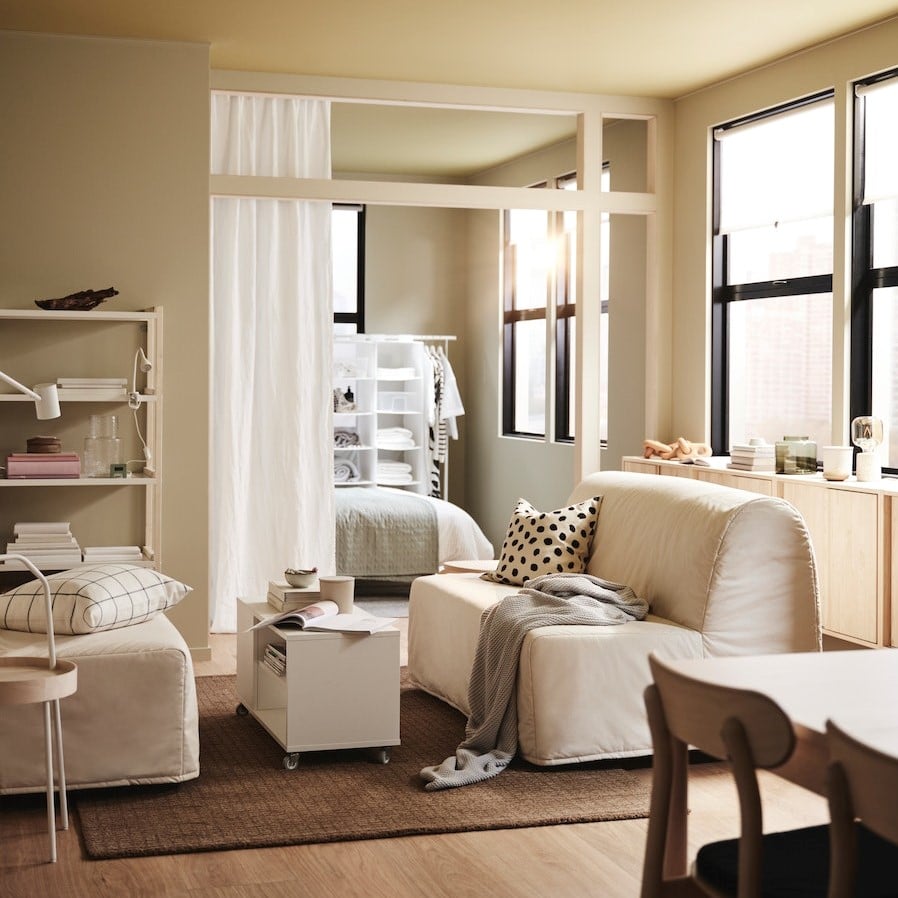 Ein Wohnzimmer mit zwei LYCKSELE LÖVÅS Bettsofas auf einem Juteteppich, u. a. mit einem VIHALS Couchtisch und einem weißen Regal.