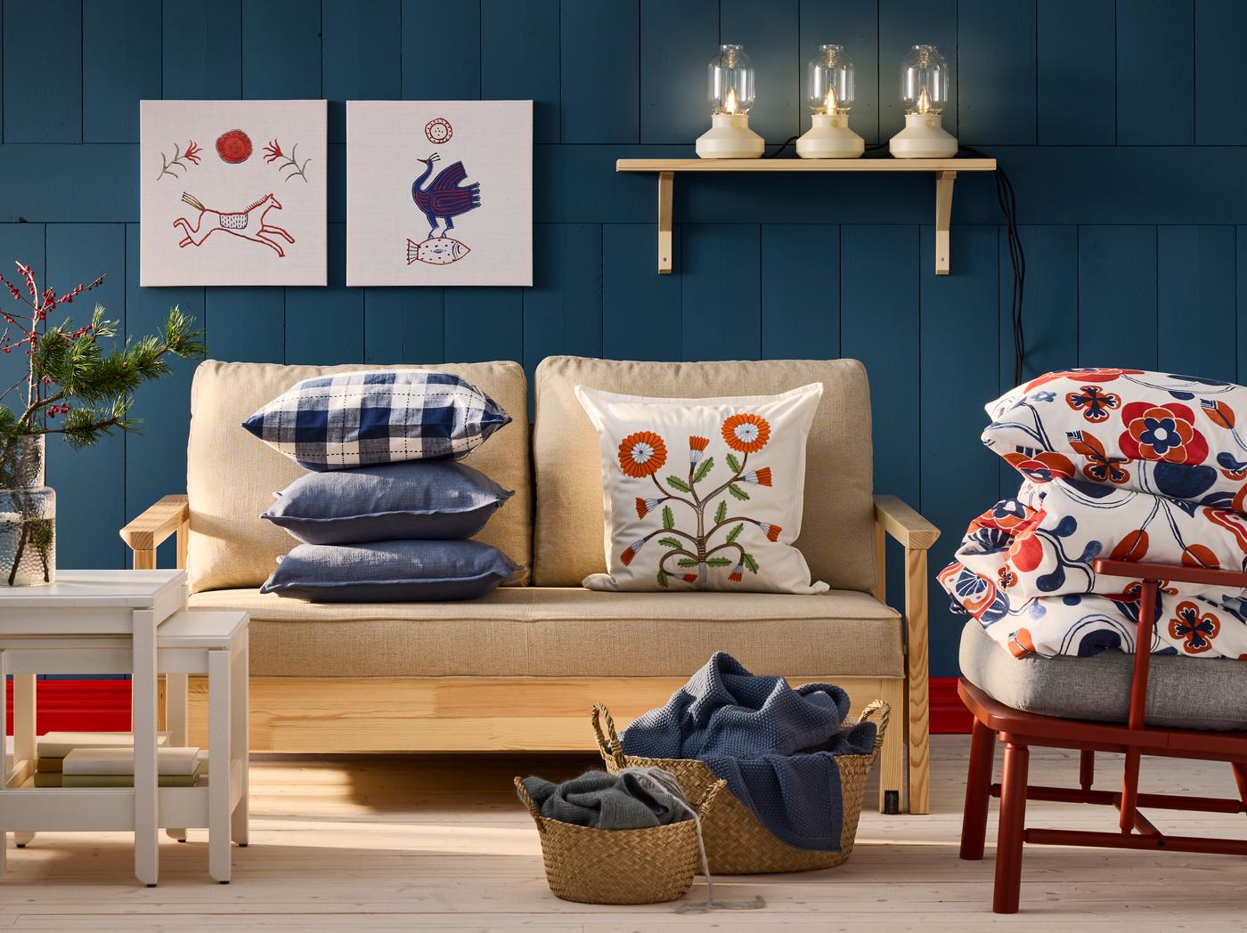 Ein Wohnzimmer, Sofa, Couchtisch, Sessel, viele Pölster, 2 Bilder an der Wand - alles in den Farben blau, rot und creme beige