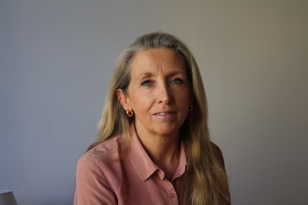 Eine blonde Frau lächelt in die Kamera, sie trägt eine rosa Bluse.