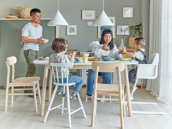 Eine Familie in einem Esszimmer, in dem mehrere RÖNNINGE Stühle aus Birke zu sehen sind. Die Mutter und die zwei Kinder sitzen am Esstisch, während der Vater eine Schüssel zum Tisch trägt.