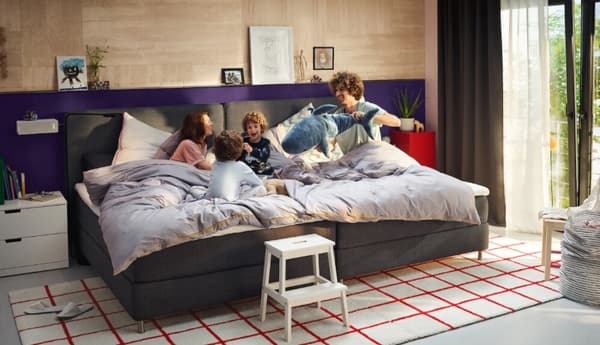 Eine Familie mit Mama, Papa und zwei Kindern spielen mit Stofftieren in einem Familienbett von IKEA