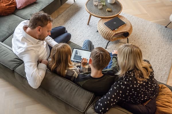 Eine Familie sitzt gemeinsam in Wohnzimmer auf der Couch und informiert sich über IKEA.