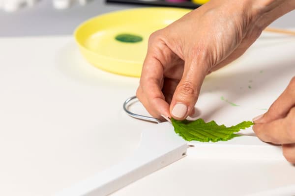 Eine Frau drückt das Blatt mit der Farbe auf einen weißen Kleiderbügel