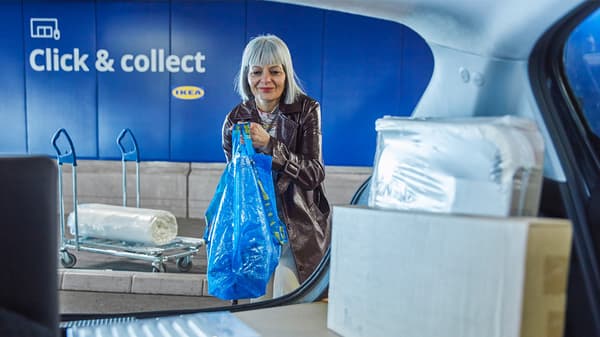 Eine Frau holt ihre Pakete aus der Click & collect Box ab und bringt sie in ihr Auto in einer blauen IKEA Tasche.