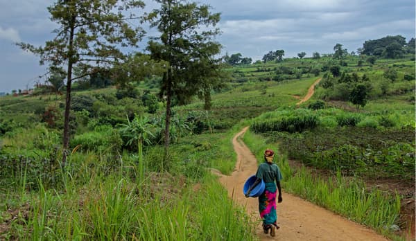 Eine Frau läuft einen Weg durch eine Landschaft in Uganda entlang.