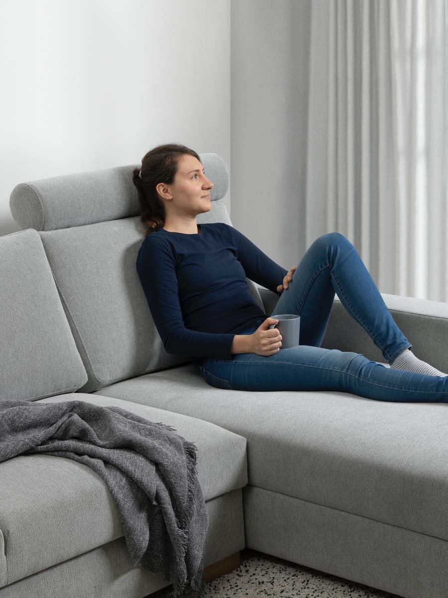 Eine Frau liegt auf einem SÖRVALLEN Sofa mit Nackenstütze.