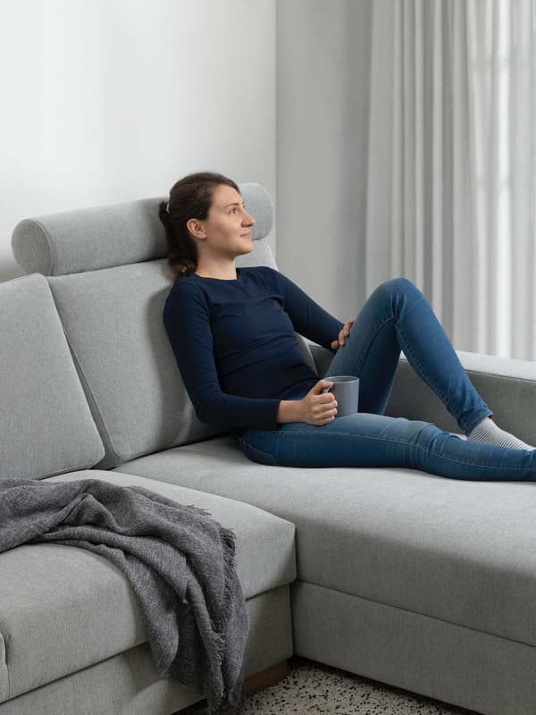 Eine Frau liegt auf einem SÖRVALLEN Sofa mit Nackenstütze. 