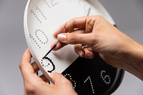 Eine Frau macht mit einer schwarzen Farbe die Zahlen auf die Uhr.