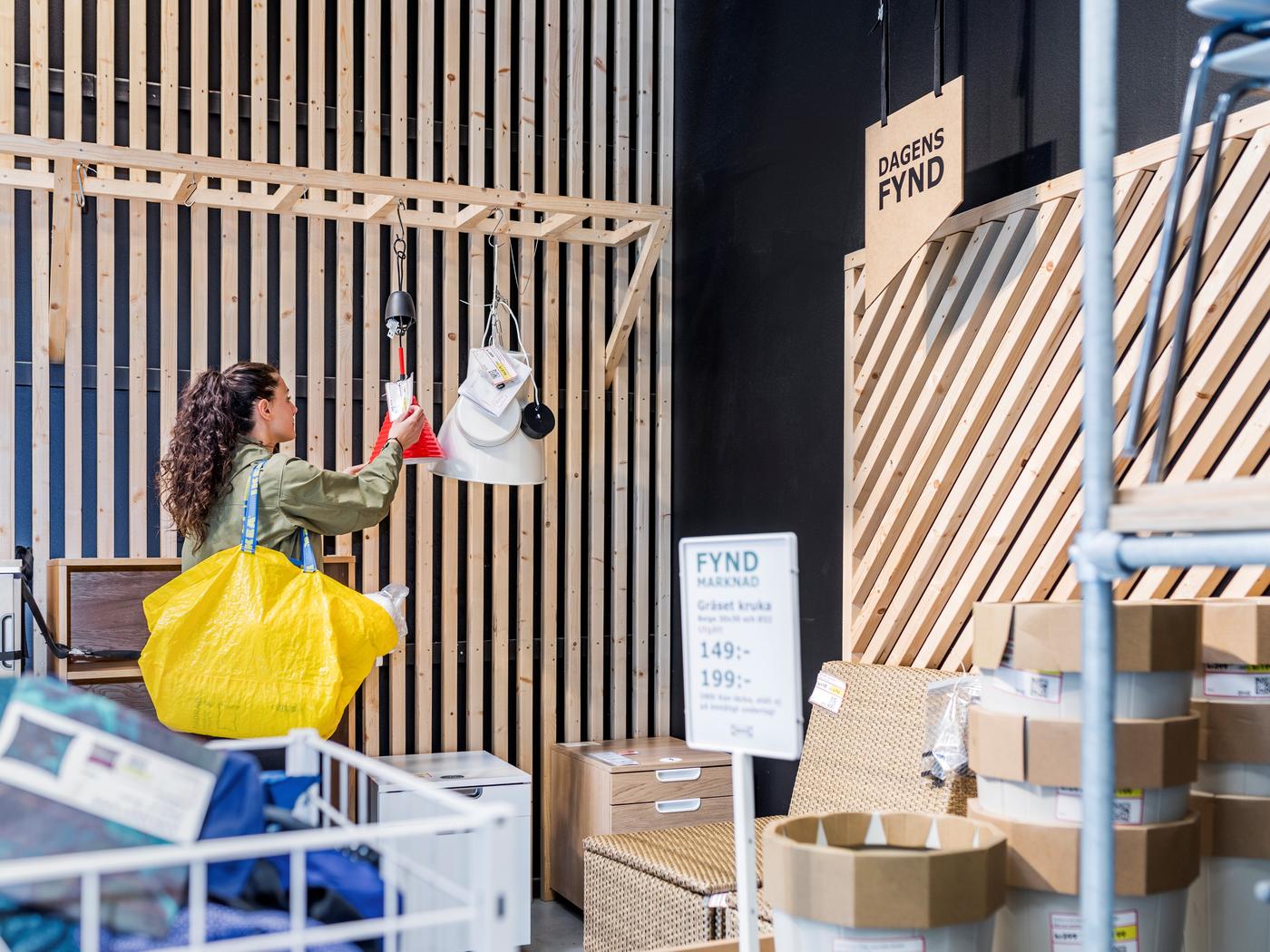 Eine Frau mit gelber Ikea Tasche steht im Zweiten Leben Shop und sieht sich Produkte an