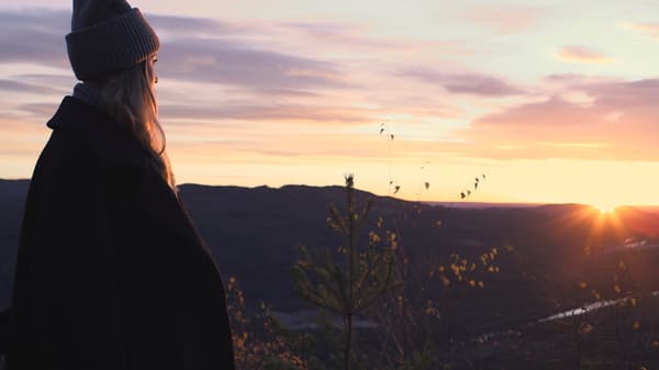 Eine Frau schaut in die Ferne der Natur und betrachtet die Sonne.
