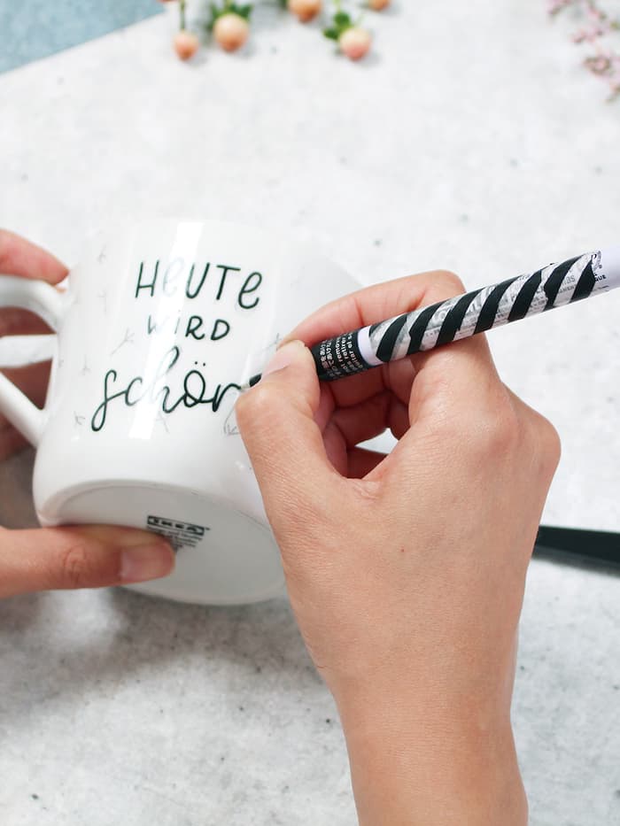 Eine Frau schreibt mit einem schwarzen Stift etwas auf eine Tasse.