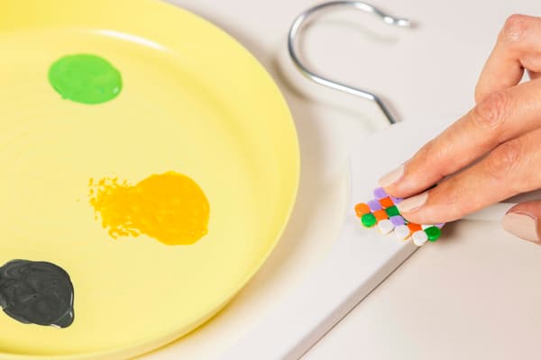Eine Frau tunkt das gebügelte PYSSLA Bügelperlen Blatt in die Farbe.