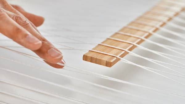 Eine Frau wicklet einen weißen Fanden um ein mittiges Holzstück.