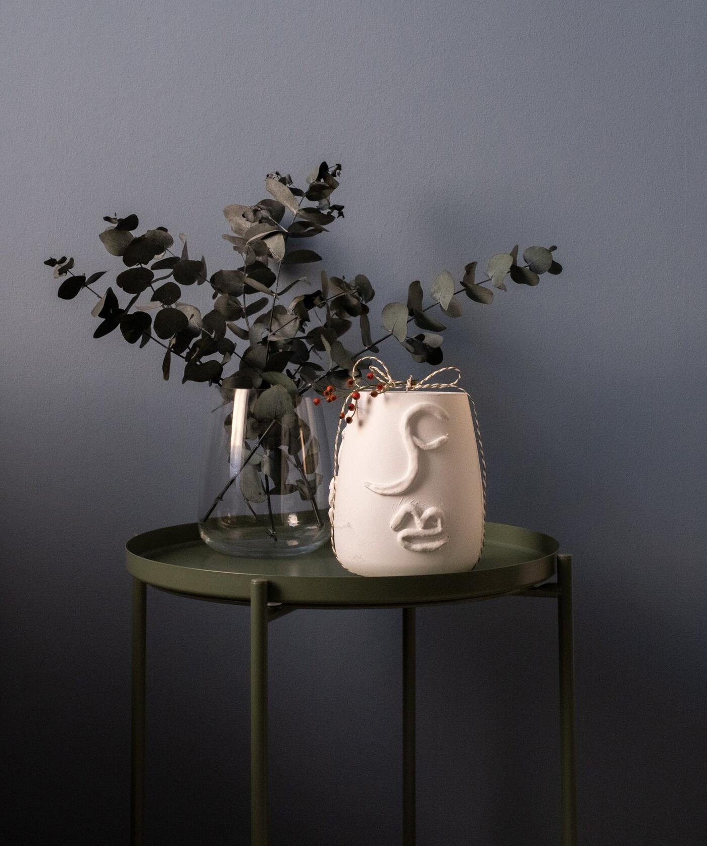 Eine Glasvase mit Eukalyptus und eine Terracota-Vase auf einem grünen Beistelltisch