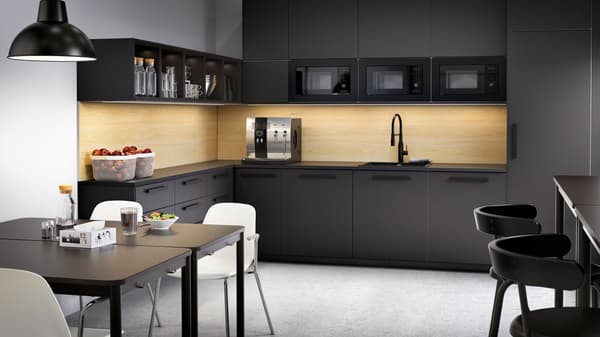 Eine große anthrazitfarbene Küche mit Schubladen und Schränken, Kaffeemaschine, Obstschalen und zwei Tischen mit weißen Stühlen.