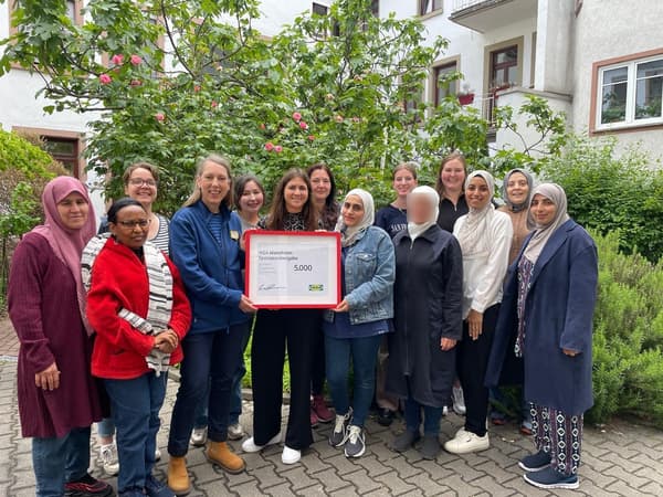 Eine Gruppe von Frauen steht in einem Garten und bekommt einen  rot rerahmnten Spendenscheck von 5.000 € überreicht