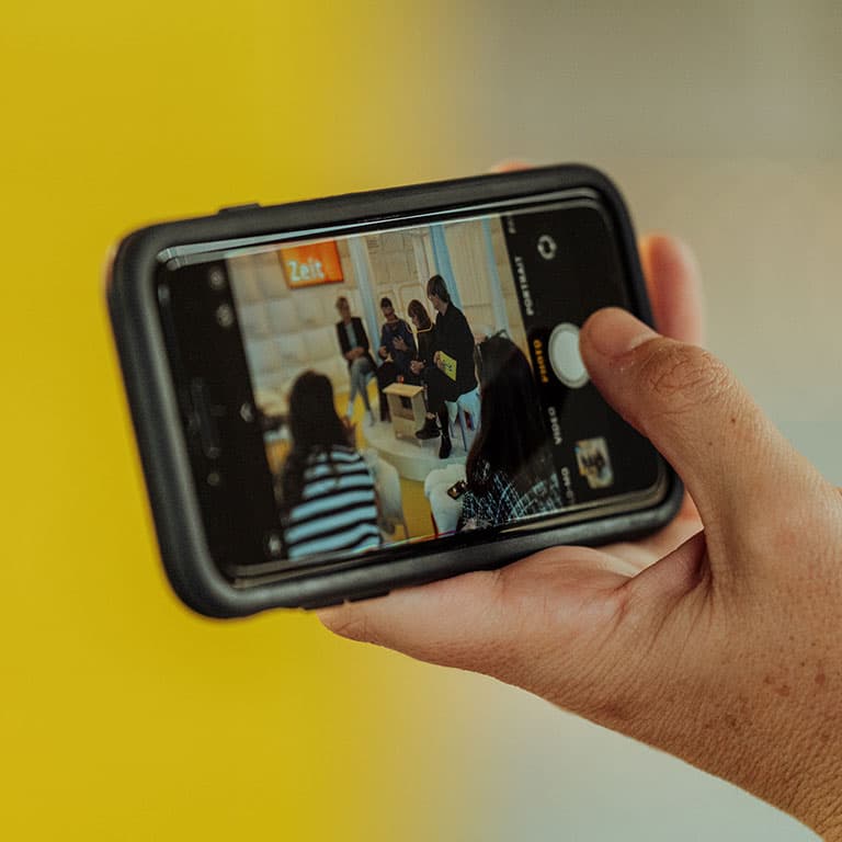 Eine Hand die ein Smartphone hällt und eine Foto von IKEA Mitarbeitern macht.