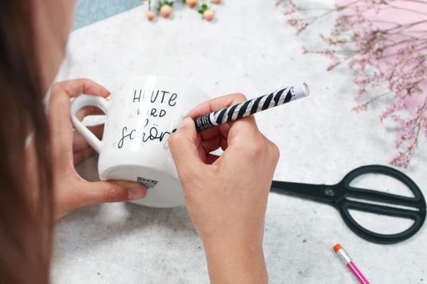 Eine Hand hält den Porzellanstift und zeichnet die feinen Linien auf der Tasse nach. 