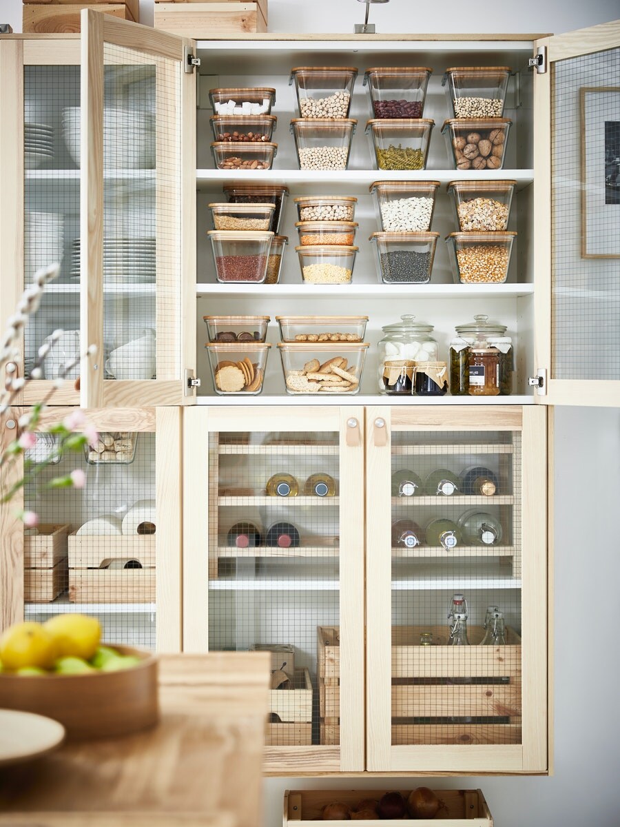 eine Hölzerne IKEA Vitrine gefüllt mit aufbewahrungsboxen im oberen Teil und im unteren Teil einige Wein Flaschen.