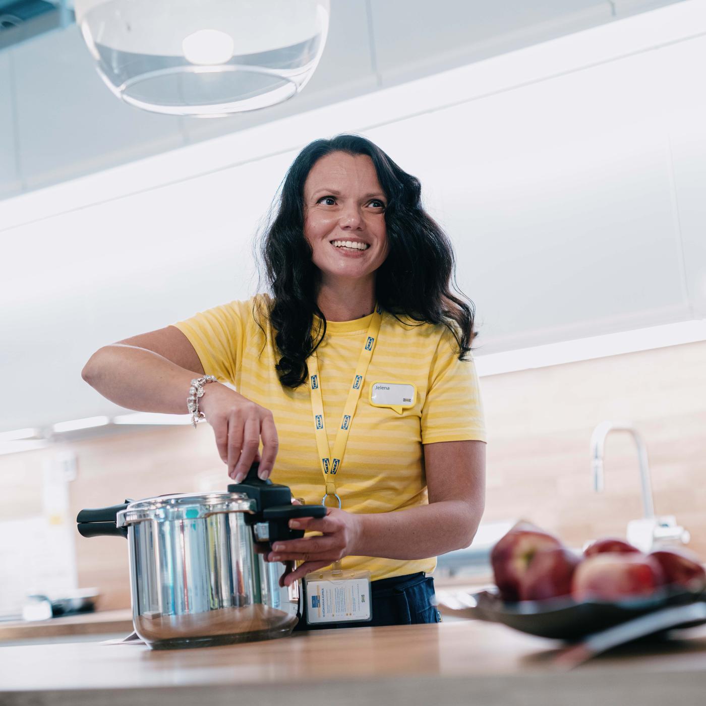 Eine IKEA Küchenplanerin in gelber Uniform zeigt wie man seine Traumküche optimal nutzen kann.