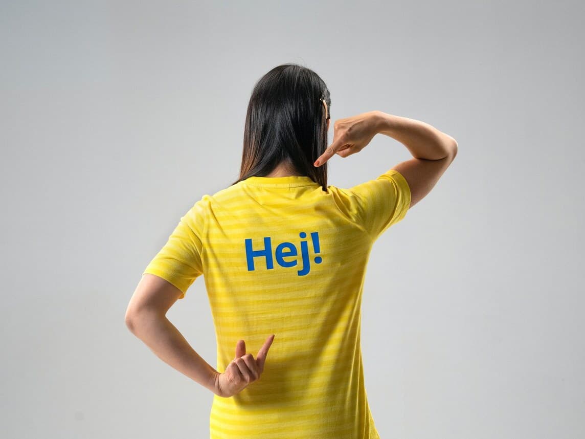 Eine IKEA Mitarbeiterin in Ihrer Dienstkleidung mit der Aufrschrift "Hej!" auf dem Rücken.