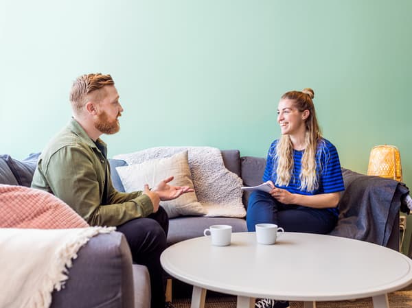 Eine IKEA Mitarbeiterin interviewt einen Bewerber, dabei sitzen sie auf einer gemütlichen Couch und trinken Kaffee. 
