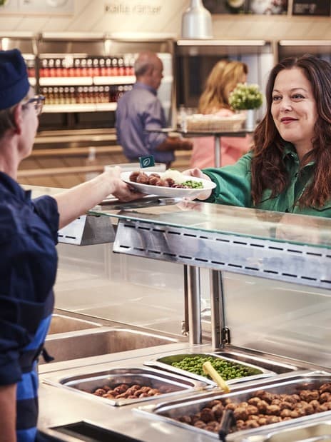 Eine IKEA Mitarbeiterin reicht einer Kundin einen Teller im IKEA Restaurant.