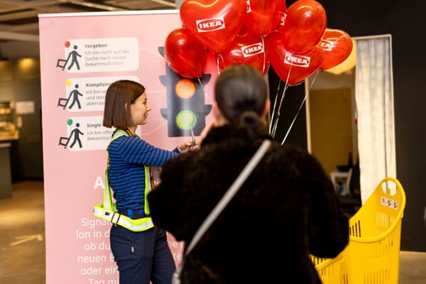 Eine IKEA-Mitarbeiterin verteilt herzförmige Ballons an eine Besucherin bei einer Aktion mit Ampelsystem.


