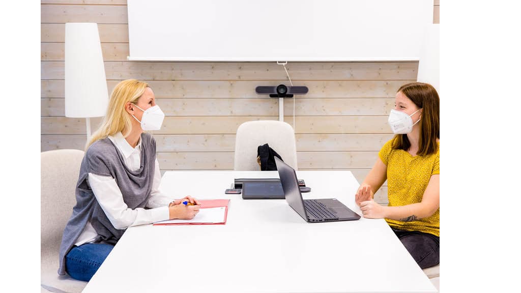 Eine Ikea Recuiterin ind Gelb führt mit einer Person ein bewerbungsgespräch in einem weißem Meetingraum