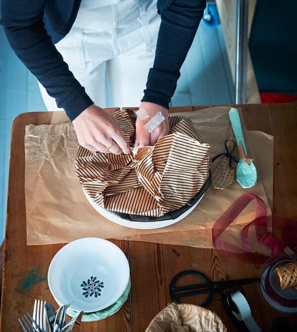 Eine Inneneinrichterin verpackt Geschirr in Geschenkpapier