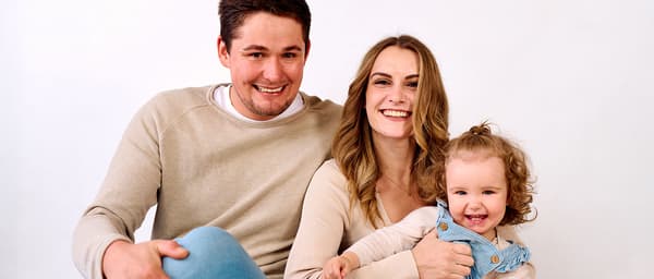 Eine junge, dreiköpfige Famile posiert mit lachenden, fröhlichen Gesichtern für's Photo-Shooting.
