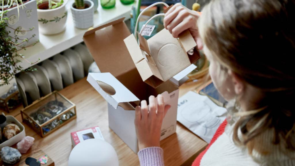 Eine junge Frau packt ein Ikea Produkt aus einem Papier Karton aus 