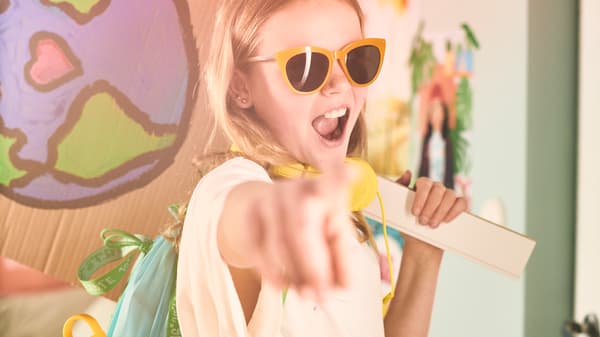 Eine junge Person mit gelber Sonnenbrille zeigt mit dem Finger auf die Kamera. Sie trägt einen BLÅVINGAD Rucksack in Blau/Grün.