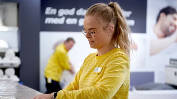 Eine junge Person steht in IKEA Kleidung an einem Tisch und verpackt etwas.