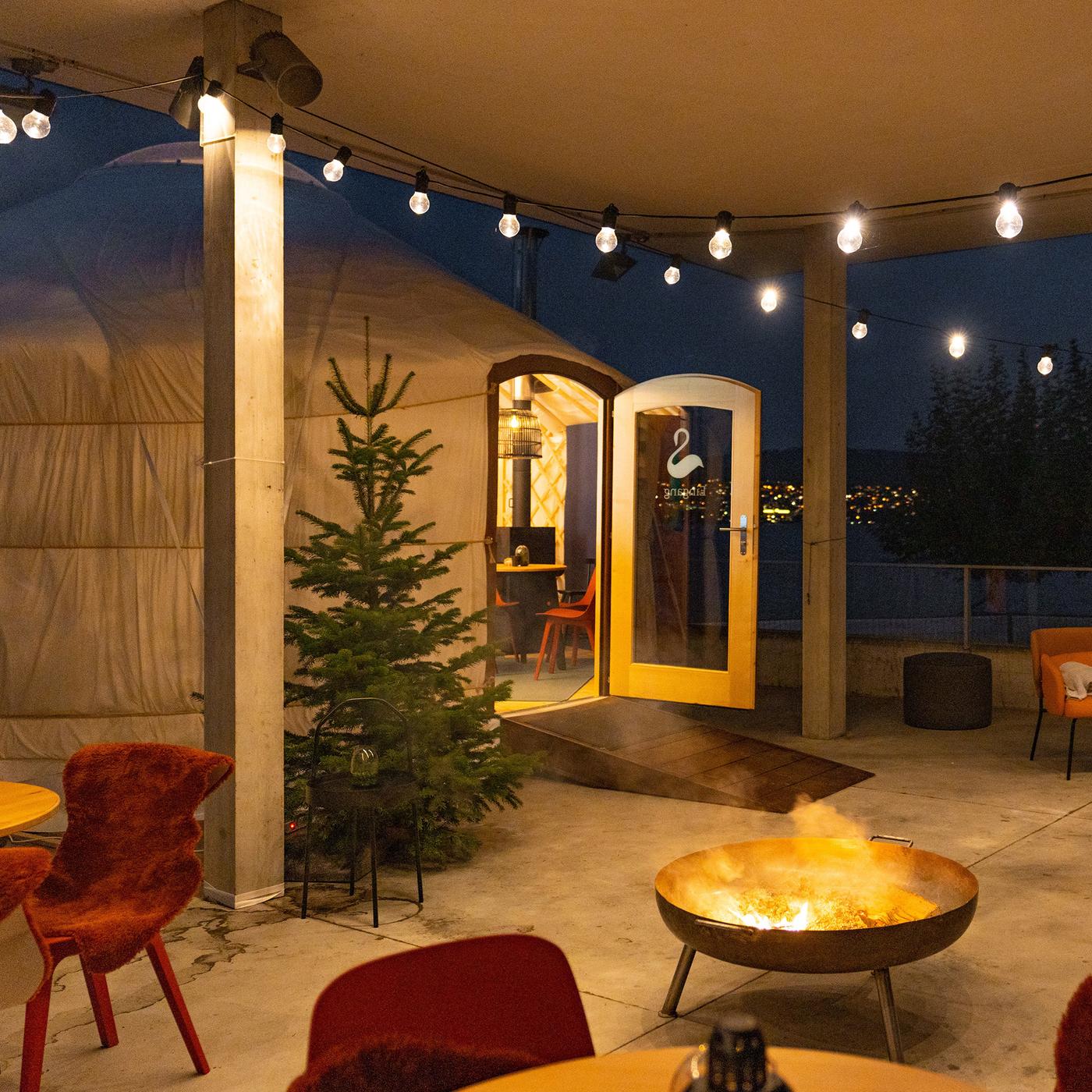 Eine Jute mit geöffneter Türe vor einer Terrasse mit Stühlen, Tischen und einer Feuerschale